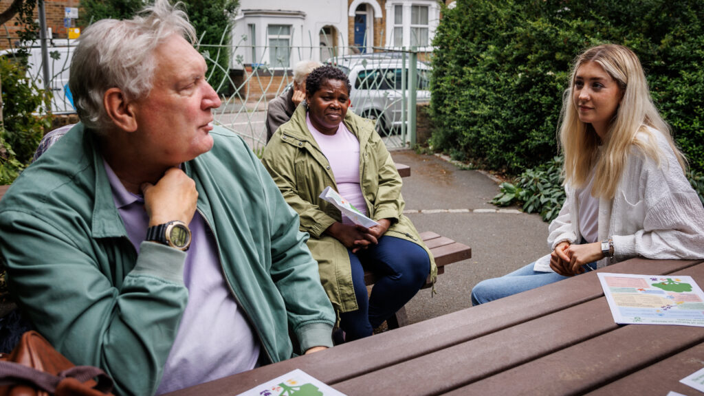 An older Guideposts member sits outdoors with other Guideposts members and staff. 