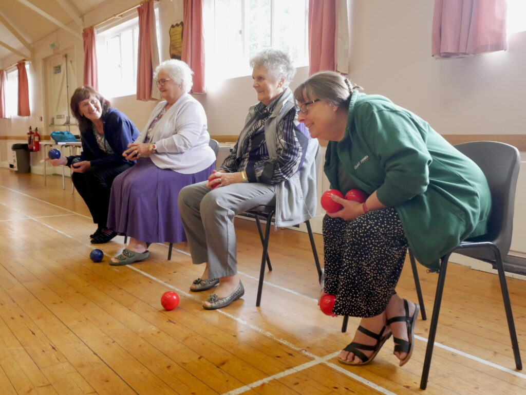 Older people sitting rolling balls as they play games at a Guideposts group.