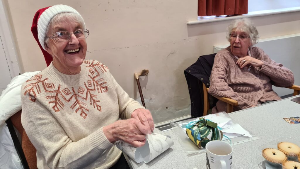 Two older ladies wearing Christmas hats enjoy mince pies at a Guideposts Connect group.