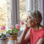 A lonely elderly lady looks out the window