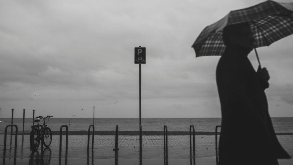 A man holding an umbrella walks across a dark and rainy road.