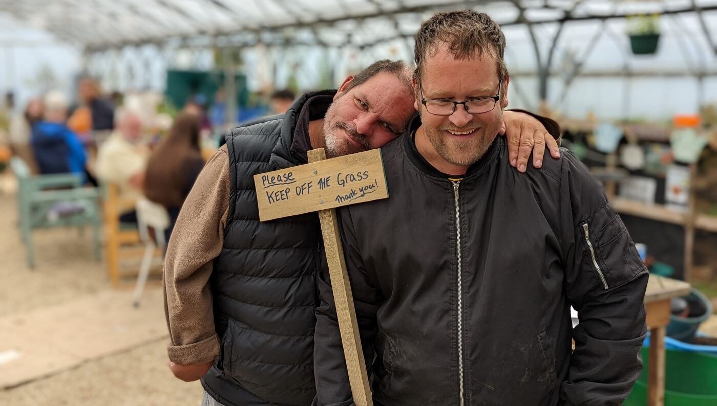 One man leaning head on shoulder of his friend. They are holding a sign saying keep off the grass.