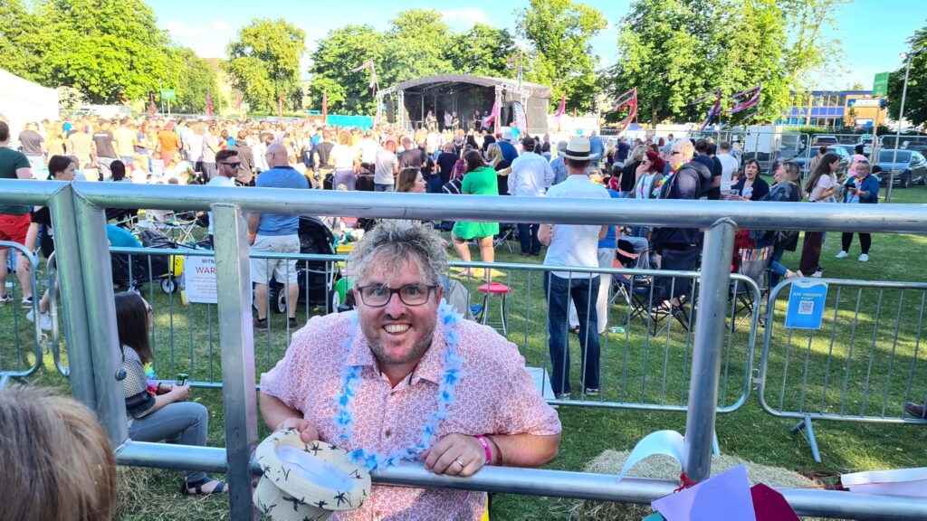 person at smiling with excitement at festival, with the main stage behind him 