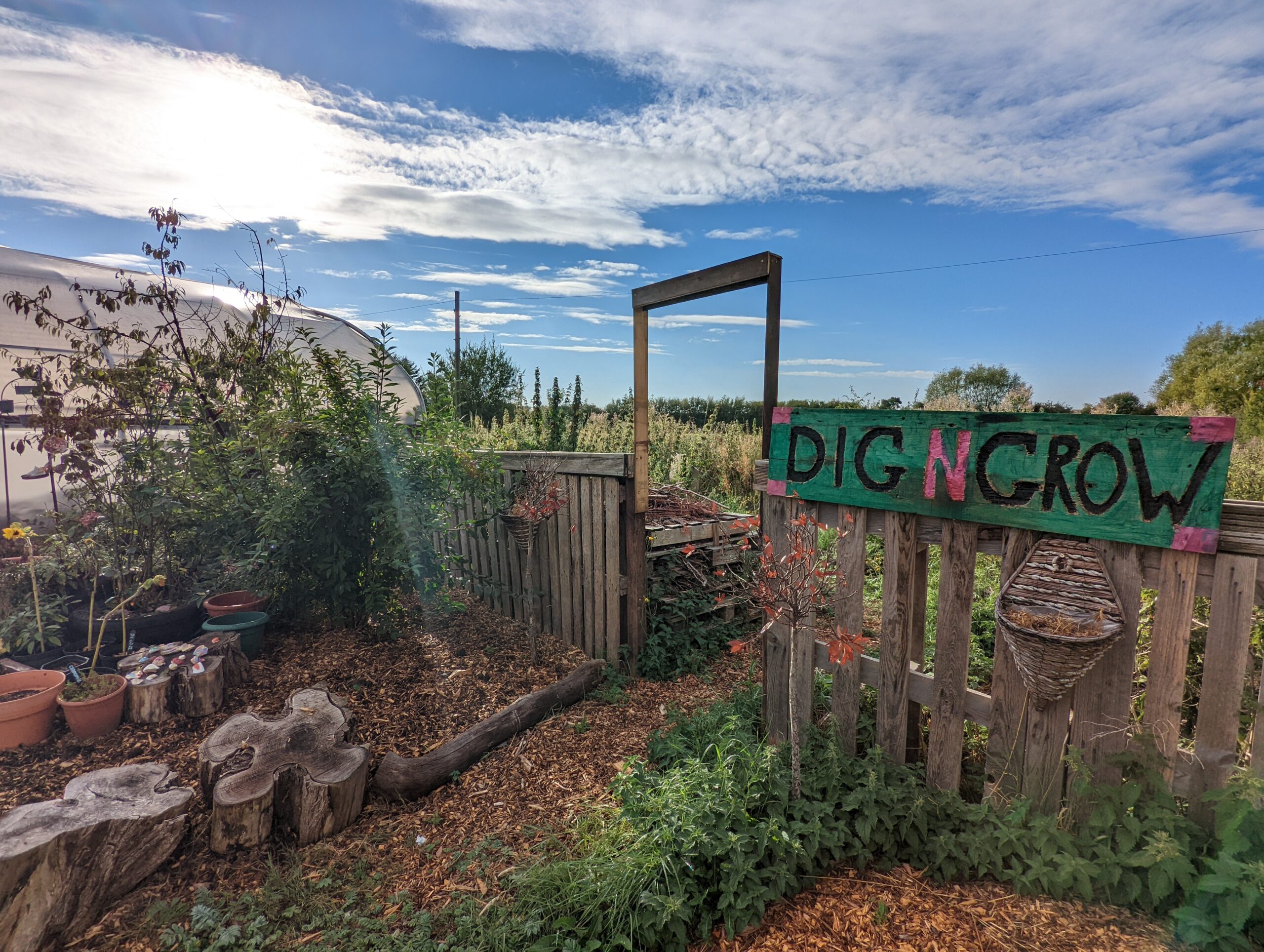 Entrance to Dig'n'Grow site with doorway, log-seats and hand-painted sign