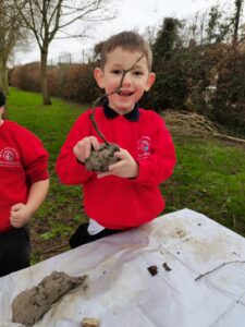 A boy in red jumper holding a sculpture he has created, and smiling excitedly.