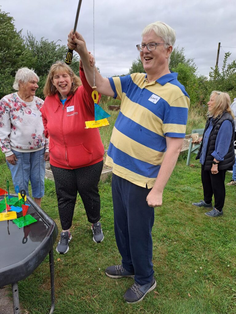 2 people smiling, having just caught a toy boat with a hook on a string