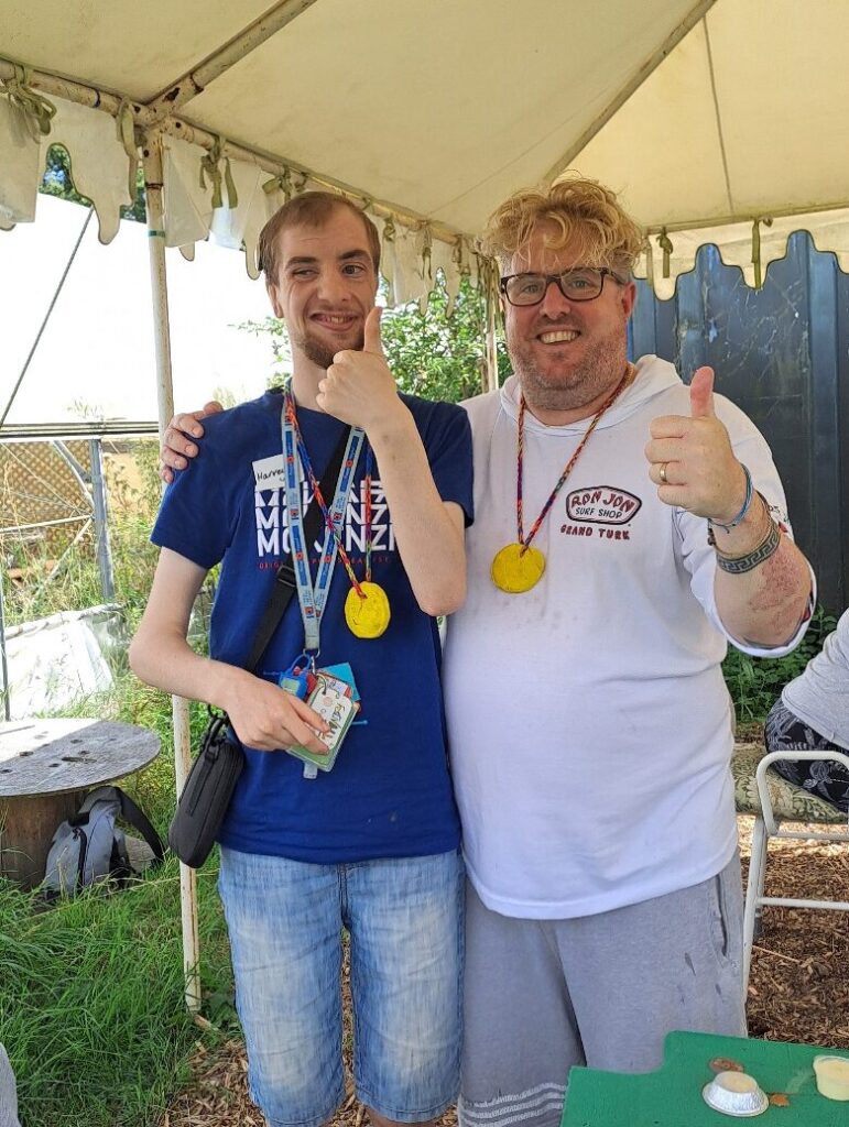 Service member and support worker looking to camera, wearing home-made medals and grinning, with thumbs up