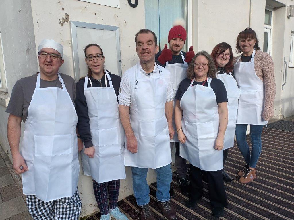 A group of people wearing white aprons and some with cooks hats on, posing for a photo with big smiles