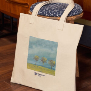 photo of a cotton tote bag lying aganst furniture. The bag has artwork printed on it of a scene with trees, on plain natural colour fabric