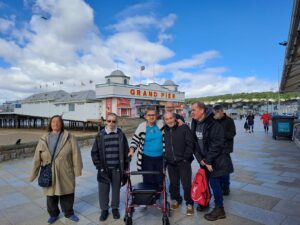 Group of people, some with disabilities, in front of the Grand Pier entrance, with blue sky and sea in the background