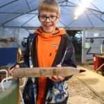 boy in orange jumper, smiling excitedly and holding a giant wooden pencil