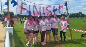 A team of 6 people under a Finish Line banner, covered in colours at the end of a colour run