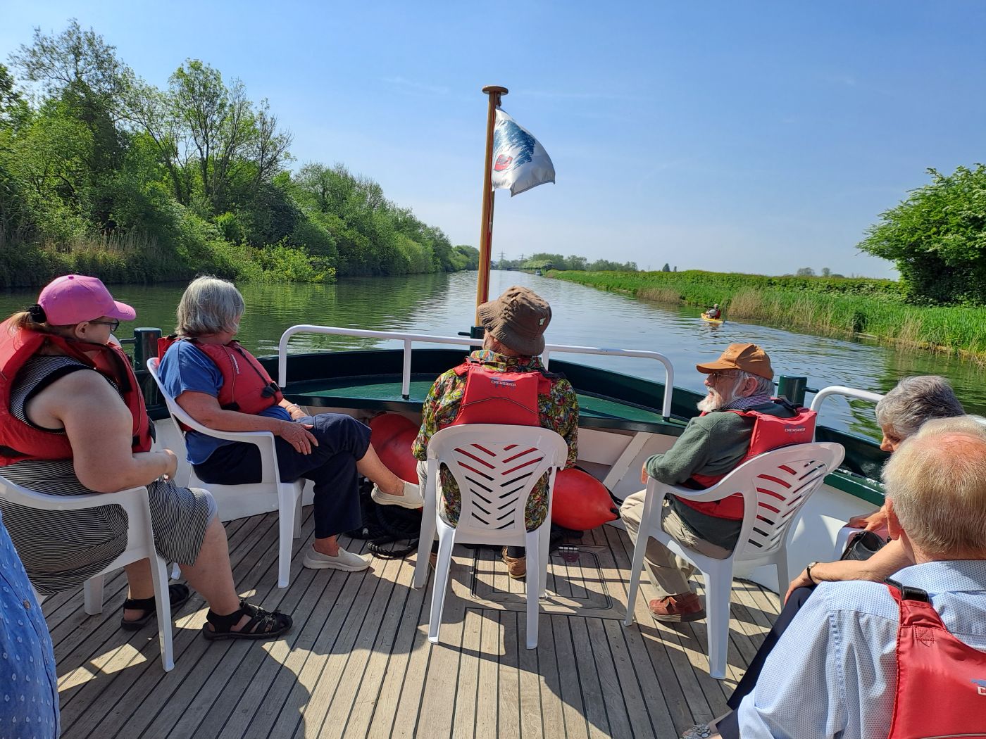 a photo of the prow of a boat as it goes down the river. There are some people on the deck, looking down the river.