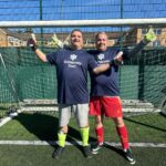 two young men in front of a football goal, wearing Guideposts Trust shirts and goalie gloves. They are smiling and have thumbs up to the side.