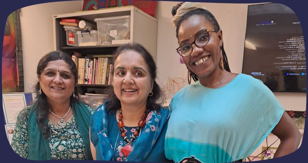 three women smiling and posing to the camera, wearing brightly coloured clothes.